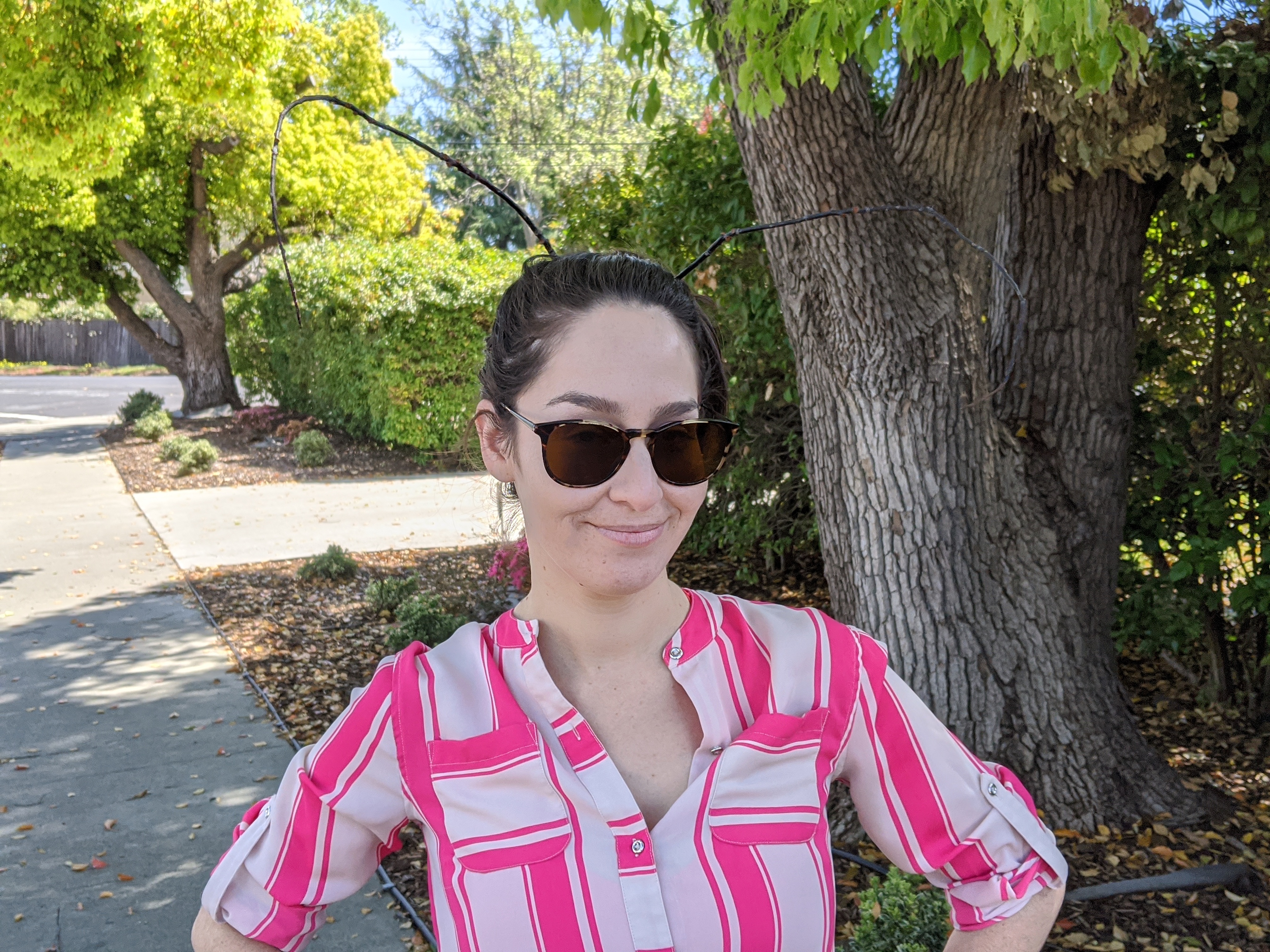 Samantha wearing sunglasses and a striped shirt on a leafy sidewalk