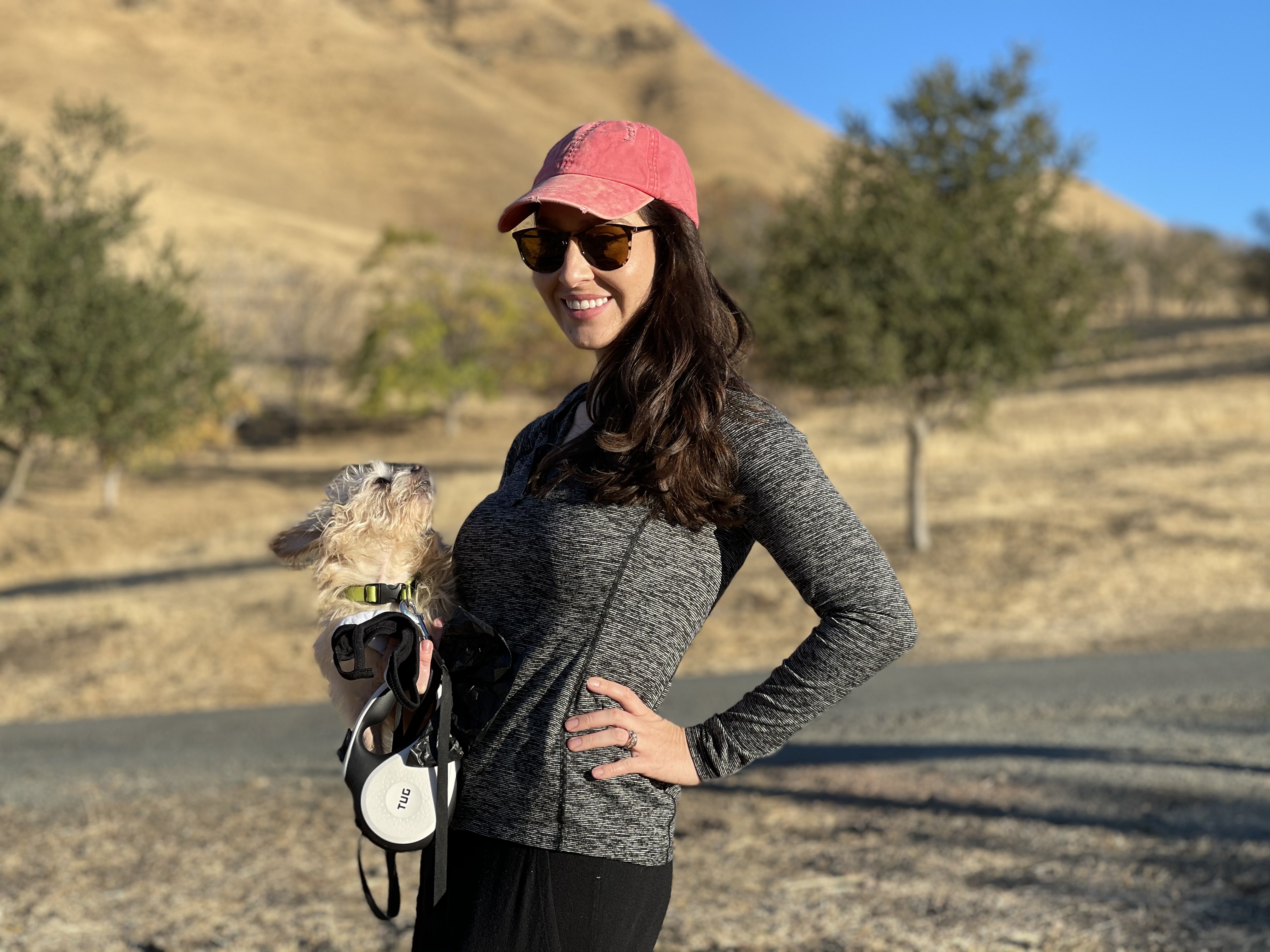 Samantha on a sunny trail with a small dog and a red cap