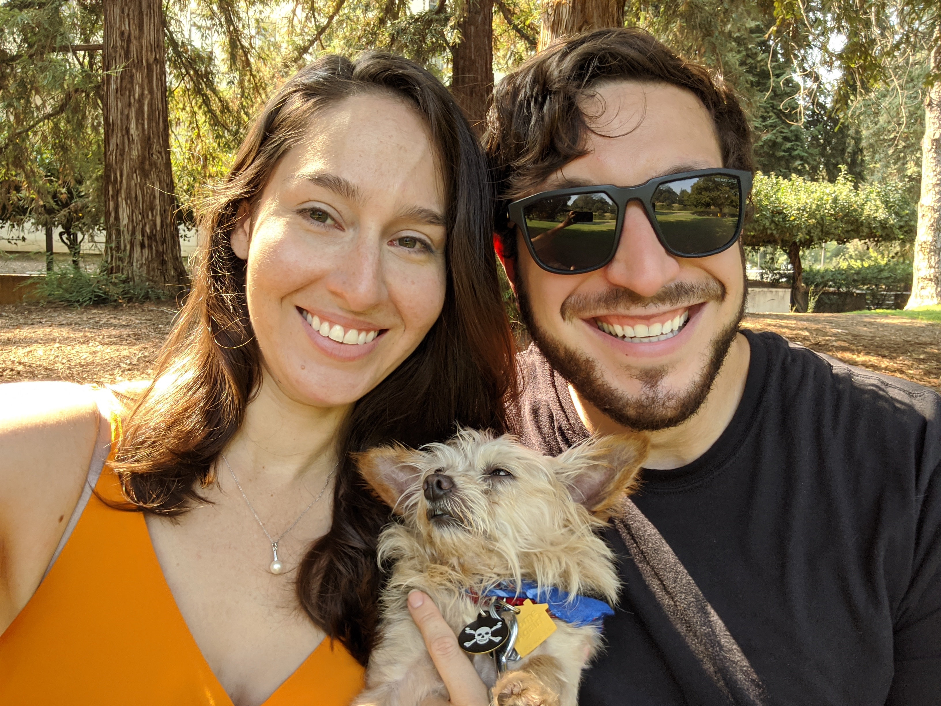 Samantha and a smiling friend with a small dog under tall trees
