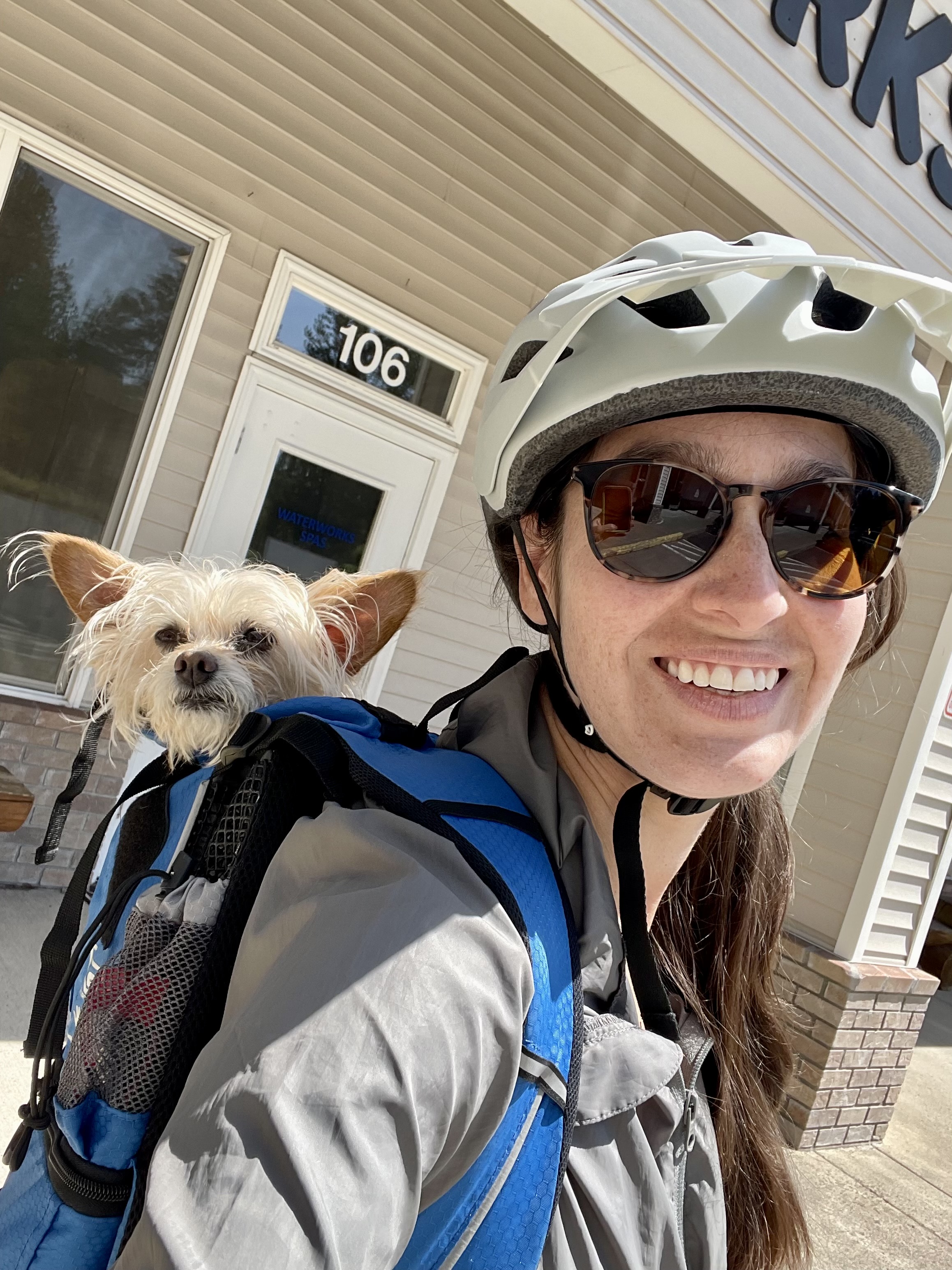 Samantha wearing a bike helmet with a small dog in a backpack carrier